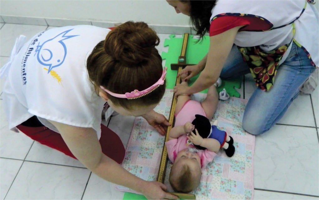voluntárias do projeto Primeiros Passos fazem medições em bebê durante atividade em creches
